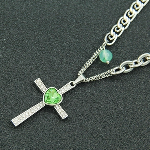 Silver cross pendant necklace with green heart gem and pave stones on black background