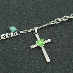 Silver cross pendant necklace featuring a green heart gemstone and white crystal inlay