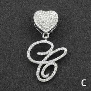 Macro shot of silver heart pendant with letter C and full rhinestone inlay on dark background