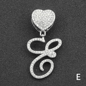Macro view of crystal encrusted silver heart clasp and cursive letter E pendant