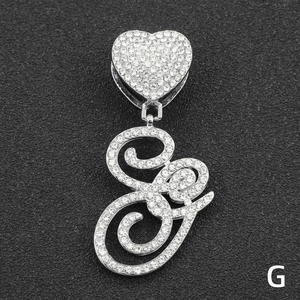 Macro detail of silver iced-out cursive letter G pendant with a sparkling heart clasp