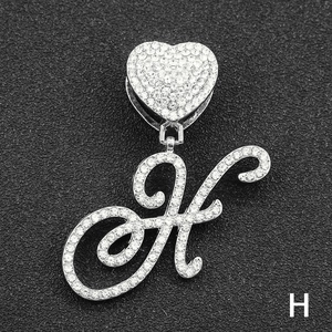Close-up of iced out silver letter H pendant with heart bail on black background