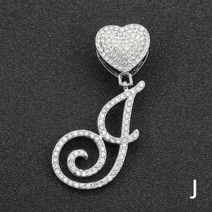 Macro shot of silver letter J pendant with full diamonds and heart clasp on black surface