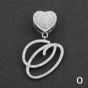 Macro detail of iced-out silver letter O pendant with heart buckle on Cuban chain