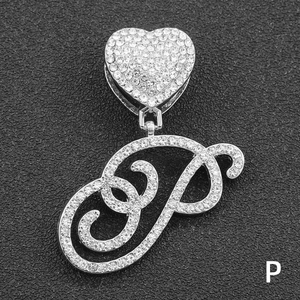 Macro detail of iced-out letter P pendant with heart-shaped bail on black background
