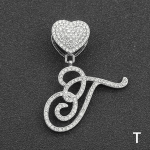 Close-up of sparkling iced out letter T pendant with heart clasp on black texture