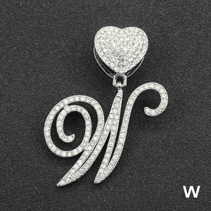 Close-up of iced out cursive letter W pendant with heart clasp on black texture