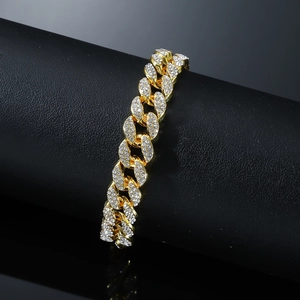 Iced out gold Cuban link anklet with shimmering crystals on a black display stand