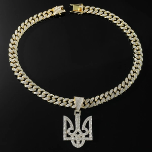 Macro shot of iced-out gold Cuban chain with a trident pendant on black background