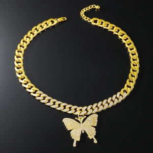 Dettaglio macro della collana cuban link dorata con ciondolo a farfalla su sfondo nero