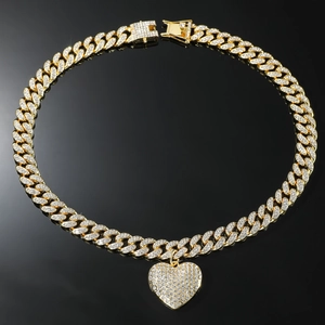 Detail van gouden Cubaanse schakelketting met grote hartvormige hanger op zwarte spiegelplaat