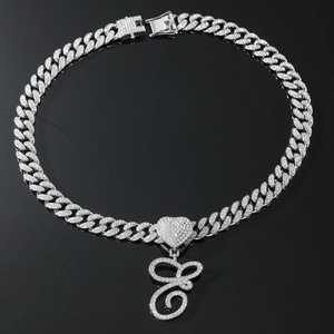 Detail of silver iced out Cuban chain with heart and letter G pendant on black background