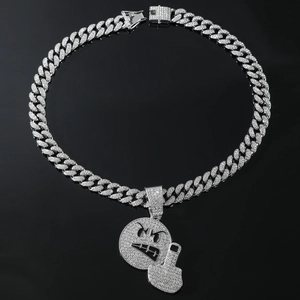 Macro detail of iced-out emoji pendant with silver Cuban link chain on black background
