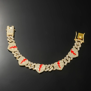 Gold Cuban chain bracelet featuring iced out broken heart charms with red enamel drip accents