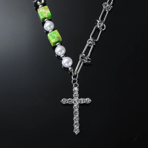Green beaded cross necklace with pearls and rhinestones on black reflective background