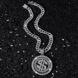 Silver iced-out Cuban link chain with a rotating dollar sign pendant on black sand