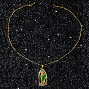 Detail of Saint Jude gold pendant with green enamel and crystal stones on black stone