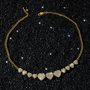 Close-up of golden hip hop heart necklace with white crystals on black stone sand