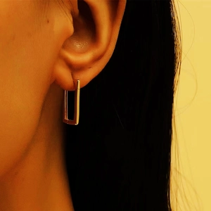 Close-up of a model wearing minimalist rectangular gold hoop earrings in S925 sterling silver