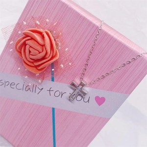 Détail d'un collier avec pendentif croix en argent posé sur un coffret cadeau rose