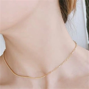 Detail of gold asymmetrical paperclip and box chain necklace on model collarbone
