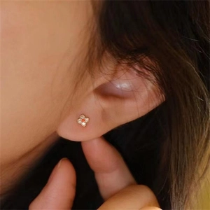 Close-up of S925 silver gold-plated clover earrings with ruby red stone on model ear