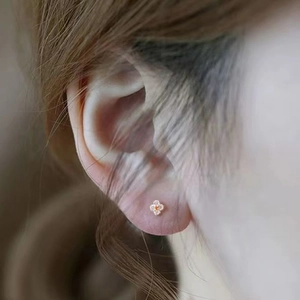 Close-up of S925 silver gold-plated clover earring with orange gem worn on ear