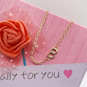 Close-up of golden letter B pendant necklace in a pink gift box with a rose flower