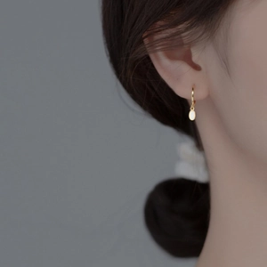 Close-up of minimalist gold hoop earring with oval white opal pendant on female model
