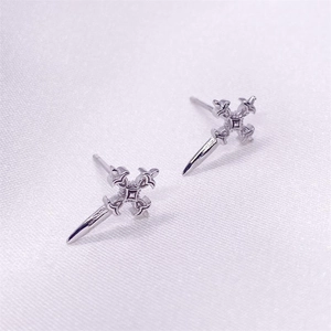 Detail view of silver S925 cross dagger earrings on a white silk fabric background