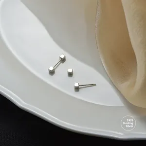 Detailed view of minimalist S925 sterling silver cube stud earrings on elegant silk background