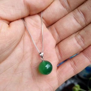 Close-up of a round green agate pendant on a silver-tone chain held in hand