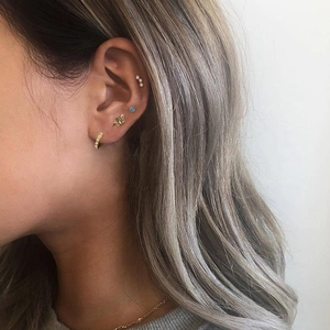 Close-up of gold star earrings and small crystal studs on model's ear showing multiple piercings
