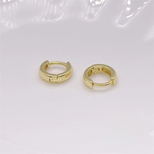 Gros plan de boucles d'oreilles huggie dorées en argent S925 sur base céramique