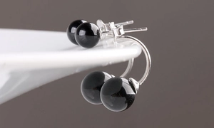Macro shot of minimalist black onyx ball earrings with polished silver studs on white ceramic