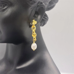 Detail of long gold chain earrings featuring white baroque pearl on a black model bust