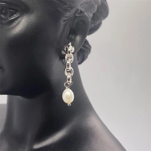 Macro shot of silver chain drop earrings with white baroque pearl on a model