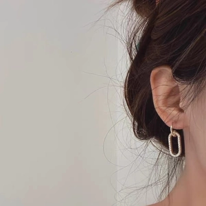 Close-up of a model wearing a gold oval drop earring with micro-paved crystal accents
