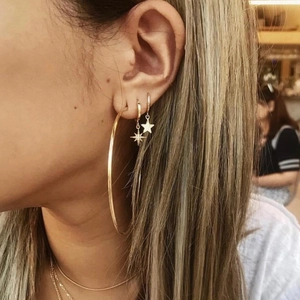 Close-up of golden hoop earrings set with star pendants worn by a female model