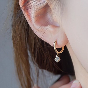 Close-up of golden S925 sterling silver hoop earring with sparkling zircon pendant on ear
