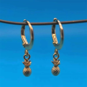 Close-up of golden pineapple hoop earrings with textured cross-grid finish on blue background