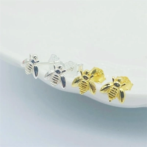 Detailed view of silver and gold bee earrings with S925 hallmarks on ceramic plate