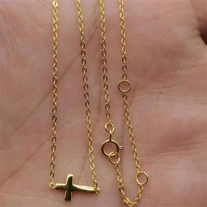 Détail d'un pendentif croix horizontale dorée sur une chaîne fine porté à la main