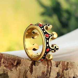 Détail d'une bague couronne dorée vintage avec strass rouges et émail noir sur bois