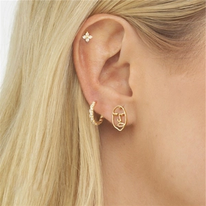 Vue détaillée de boucles d'oreilles dorées avec zircons et clou visage abstrait