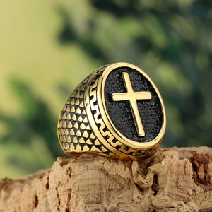 Détail de la bague chevalière croix dorée avec insert noir sur une surface en bois