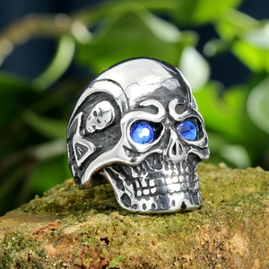 Anello a teschio in acciaio al titanio con occhi in strass blu su sfondo di pietra