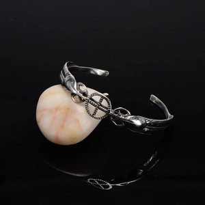 Vintage stainless steel open feather bangle with cross emblem on a light stone