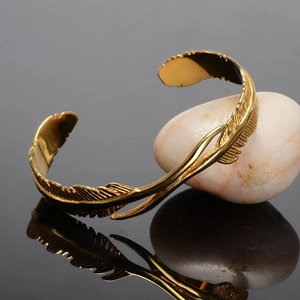 Vintage golden feather cuff bracelet in stainless steel with detailed textures on black surface
