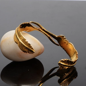 Vintage gold feather cuff bracelet made of stainless steel on dark reflective surface